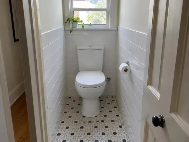 Clean white toilet in a small tiled bathroom with a window and mosaic floor in Summer Hill